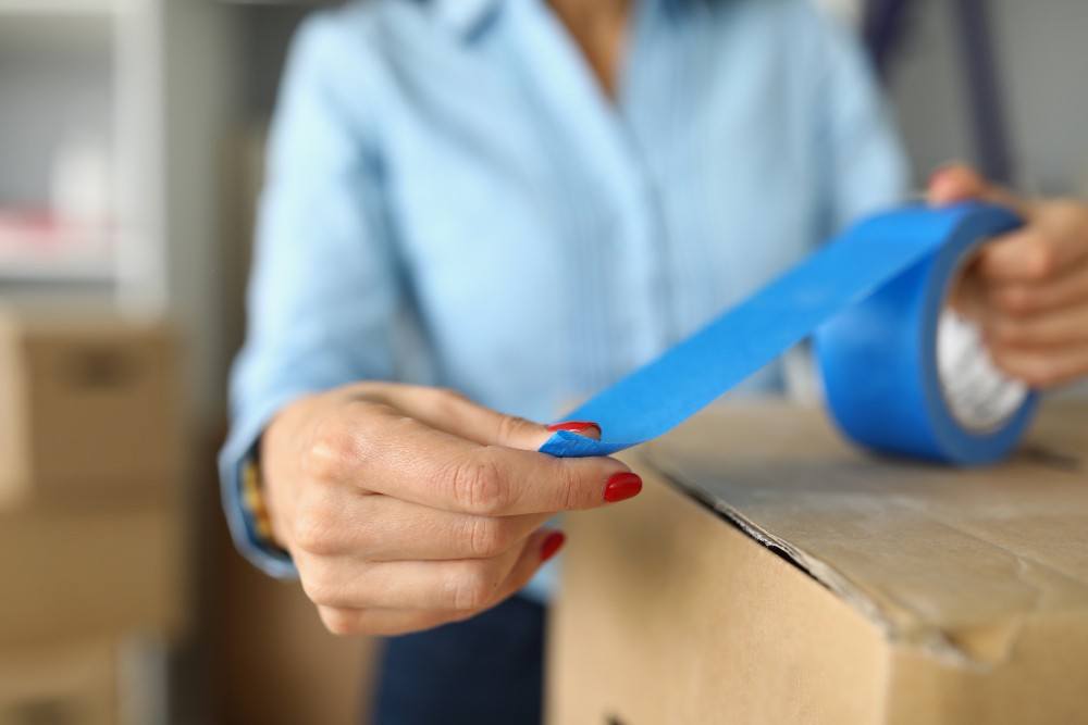 closeup female packs up things carton boxes with blue scotch woman getting ready