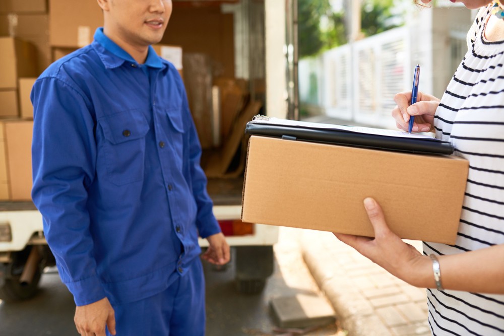 moving house company courier blue uniform looking woman signing delivery service documents