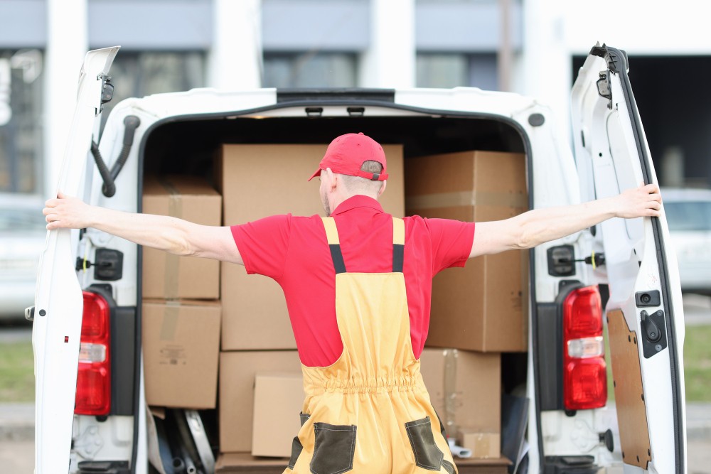 uniformed male courier opens trunk minivan filled with cardboard boxes