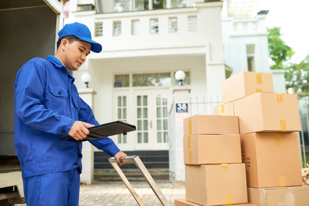 vietnamese delivery man checking information document clipboard pushing trolley with cardboard boxes